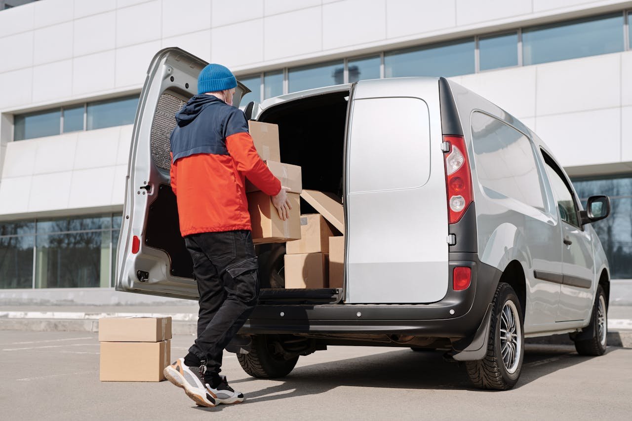 Contacto Mudanzas en Málaga. Man in colorful jacket loading cardboard boxes into a van outside an office building.