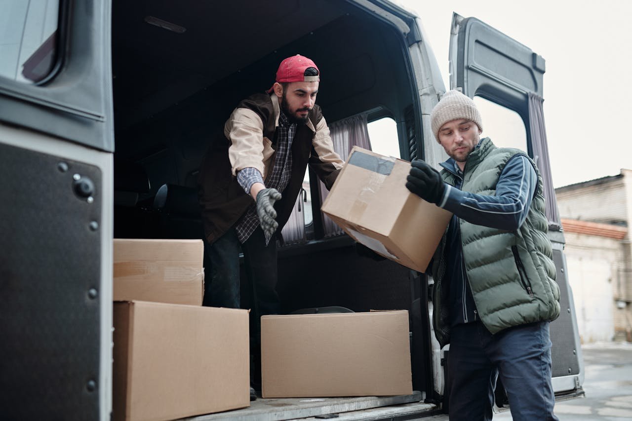 Mudanzas en Málaga. Two delivery workers unload cardboard boxes from a van, showcasing teamwork and logistics.
